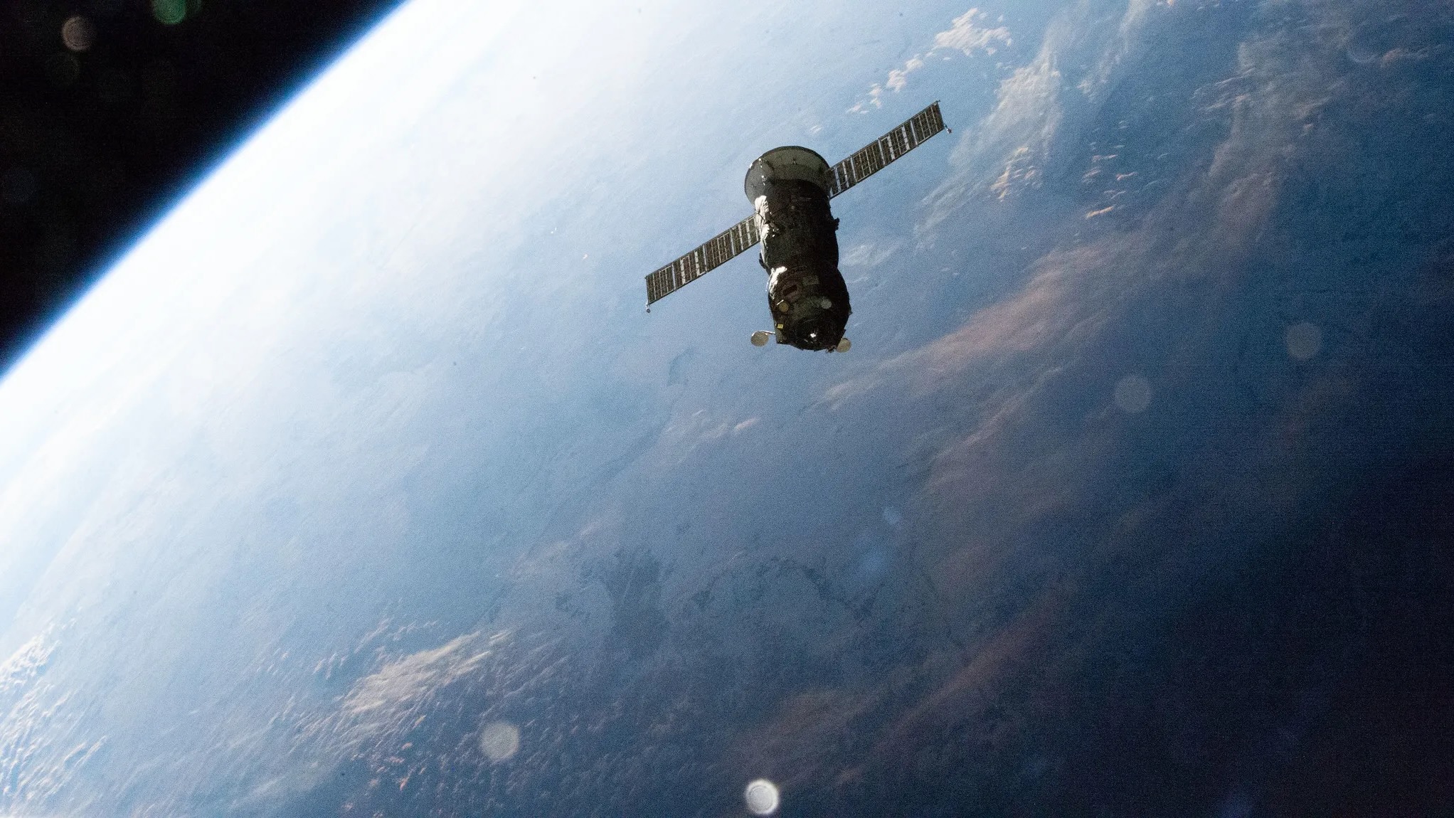An orbiting spacecraft is seen from above, with Earth in the background