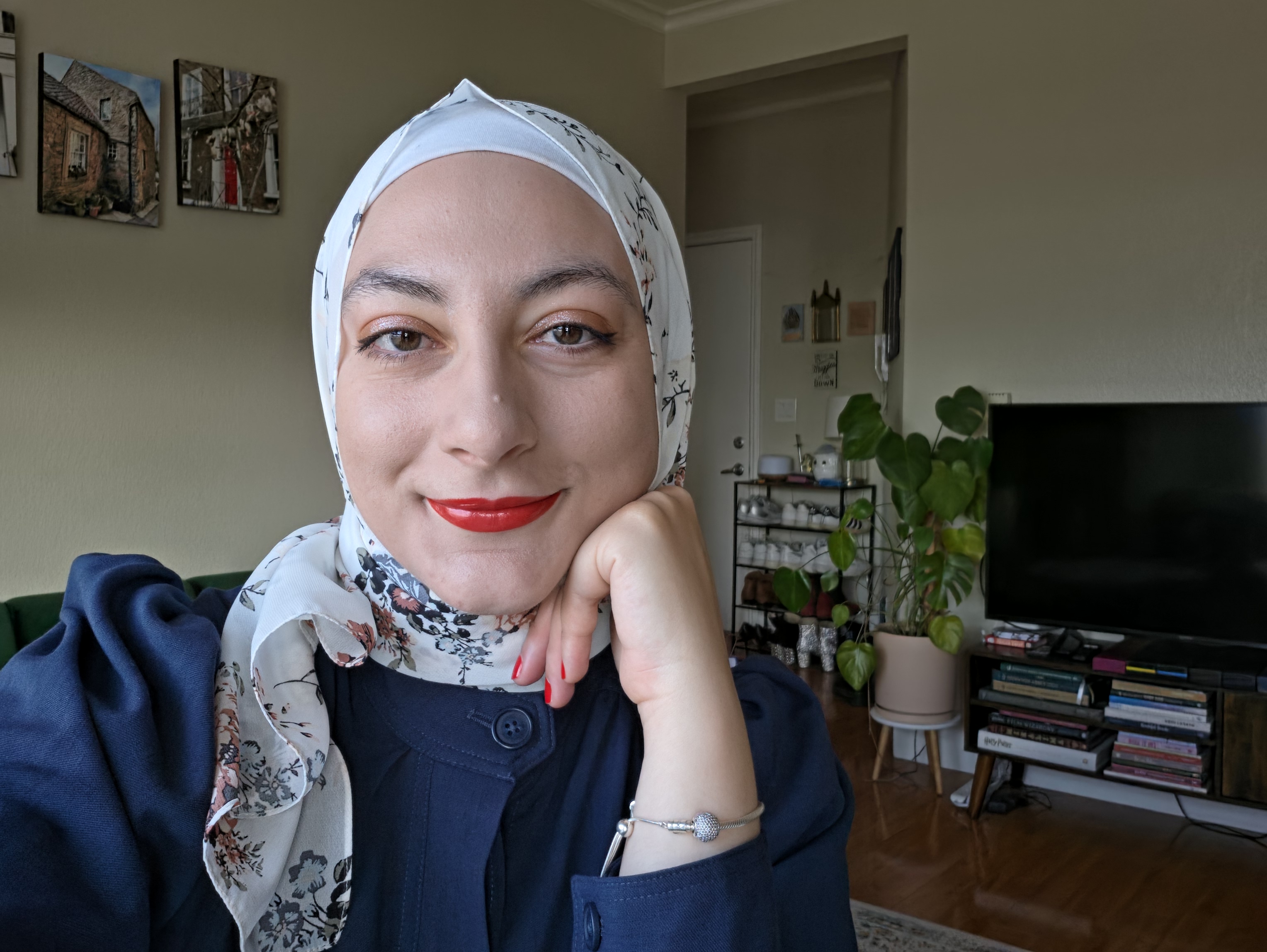 A woman in a white floral headscarf and navy shirt smiles at the camera
