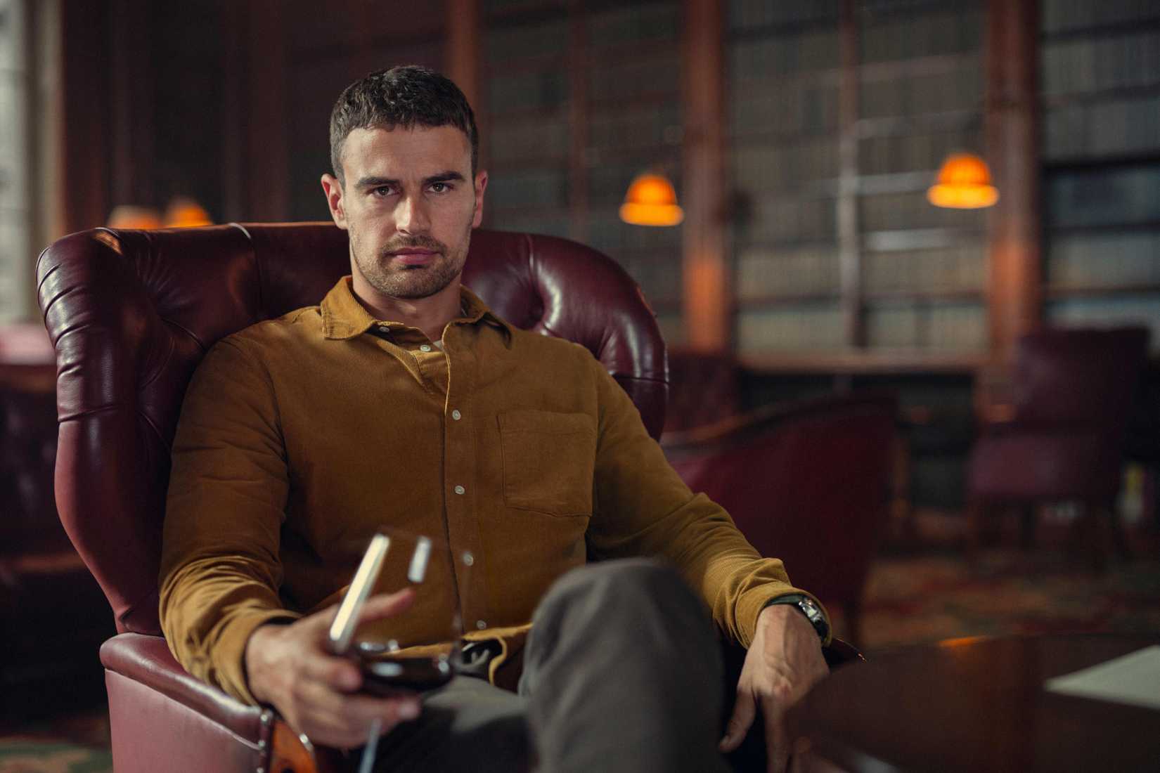 Theo James as Eddie Horniman from The Gentlemen sitting in a plush chair drinking wine