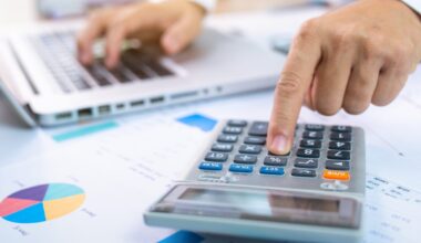 person with one hand typing on a laptop and the other working a calculator