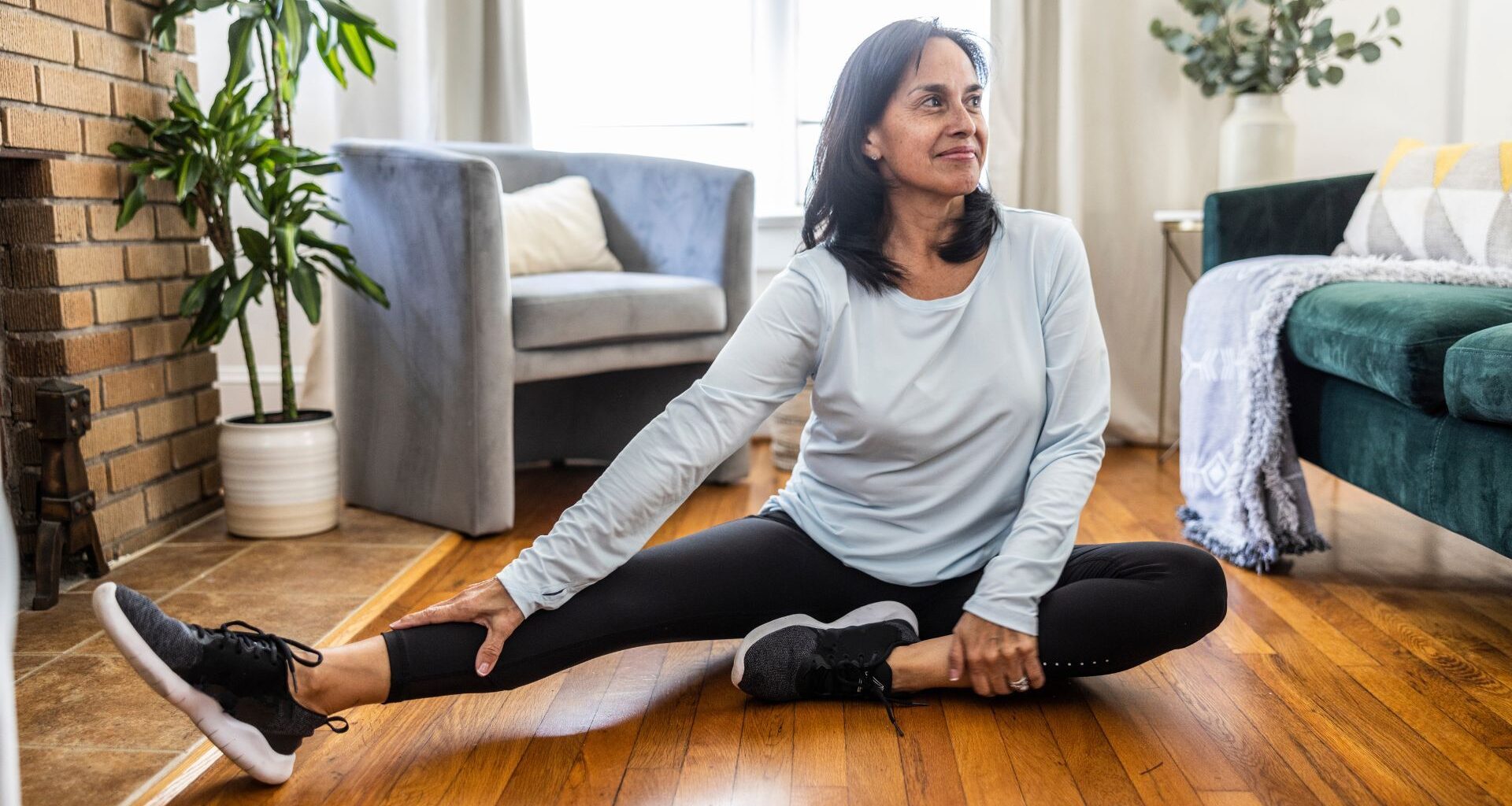 Woman stretching hamstrings on wooden floor at home to set up for Romanian deadlift exercise