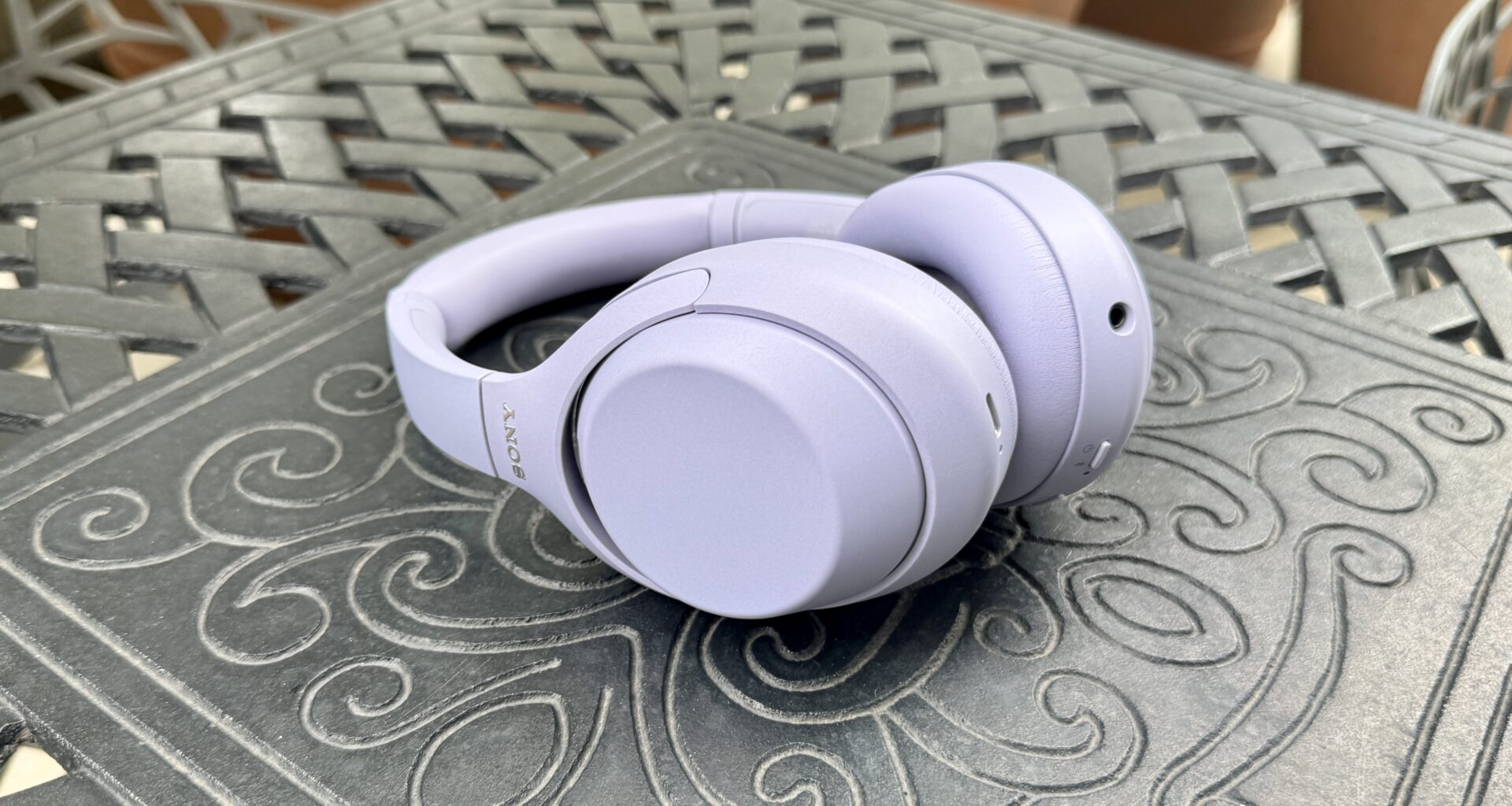 The Sony WH-1000XM4C in lavender shown lying on its side on a metal table