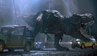 A T. rex from Jurassic Park roaring near two SUVs.