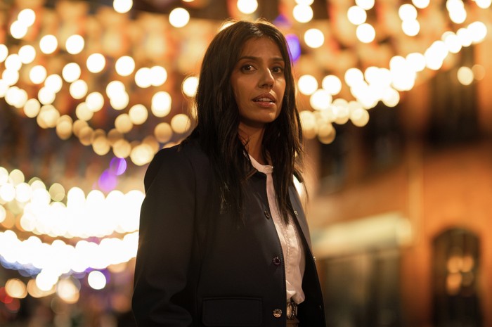 Ritua Arya in The Split Up. A woman looking into the distance with lights behind her.
