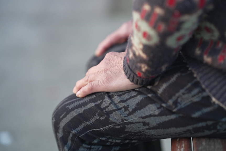 An elderly Chinese woman sitting on a bench with her hands in her lap.