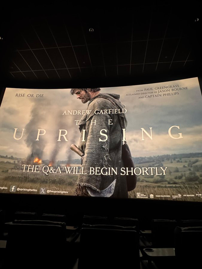 Movie screen displaying a poster for "The Uprising" starring Andrew Garfield, with text "The Q&A will begin shortly."