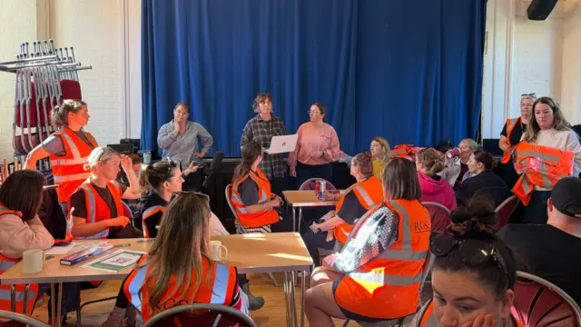 People sitting inside Brantham Village Hall listening to a briefing by Sarah Keys who is stood at the front speaking in front of the group
