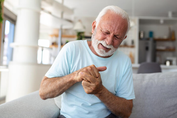 An older man in pain clutches his hand, depicting serious issues medical professionals treated from innocent signs.
