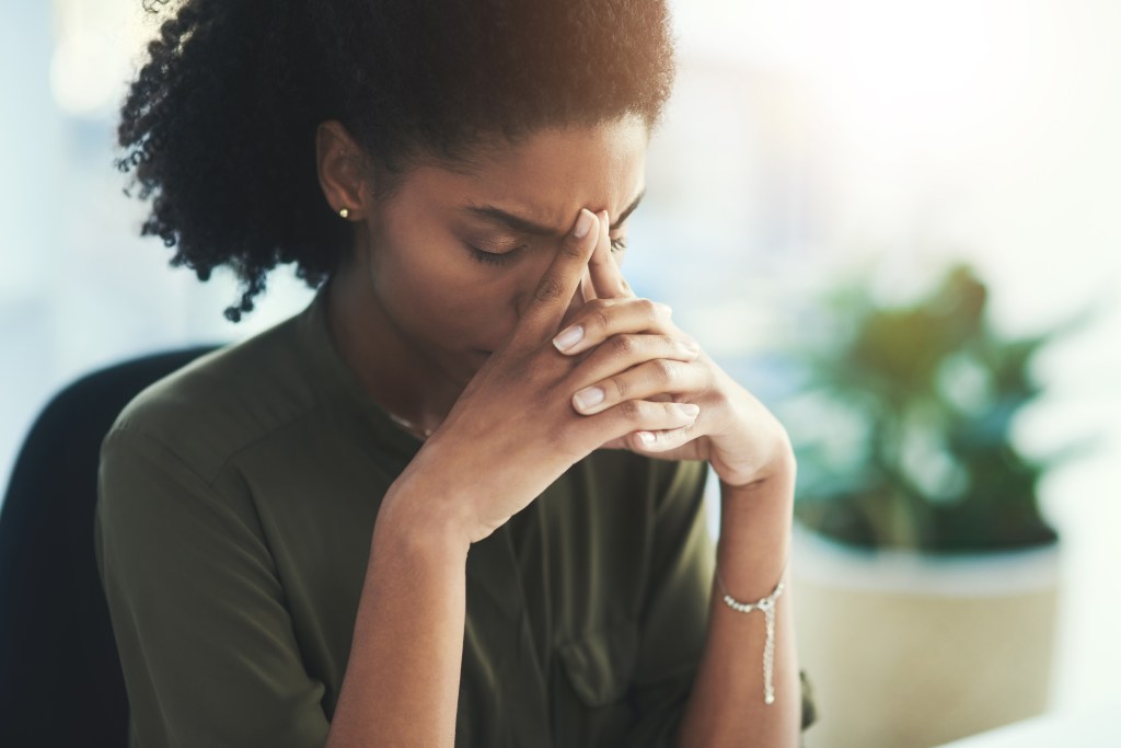 A stressed Black woman rubbing her temples, experiencing a headache or burnout.