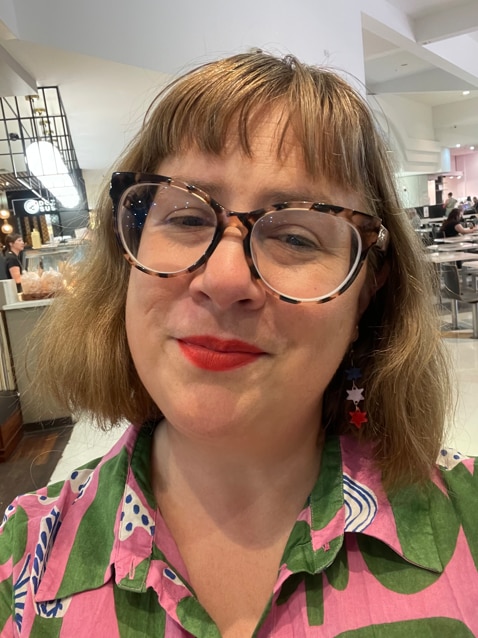 a woman with glasses and colourful top smiles