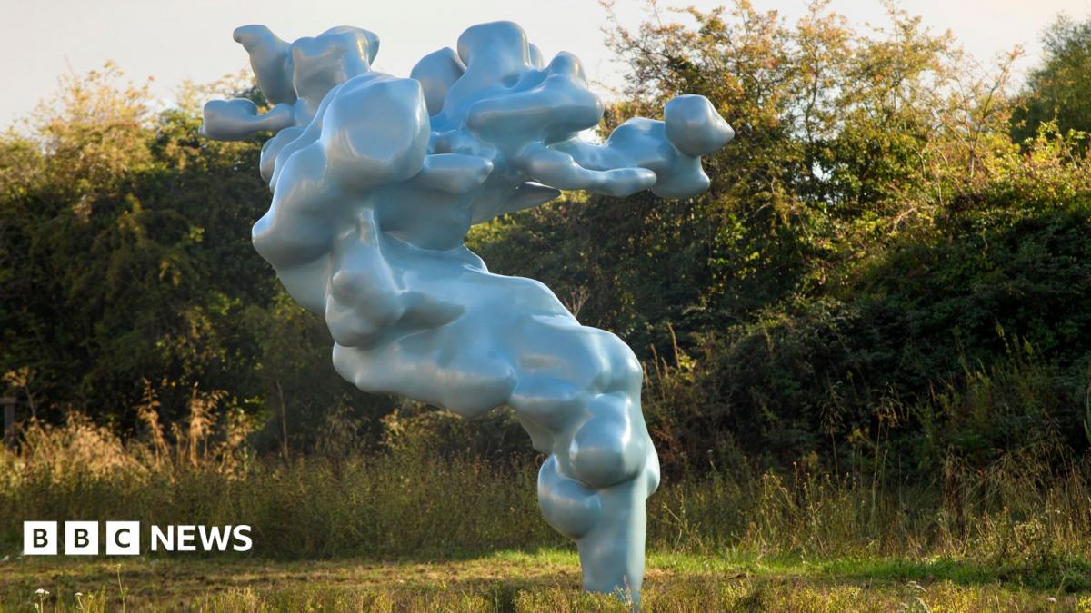 A large metallic green sculpture that is cloud-like rises out of the grass.