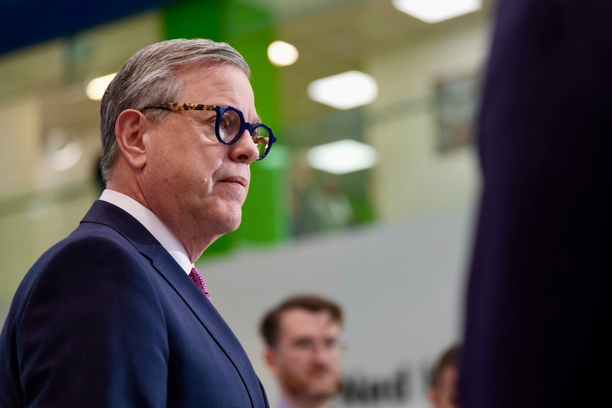 a man with grey hair and glasses speaks to reporters at a press conference