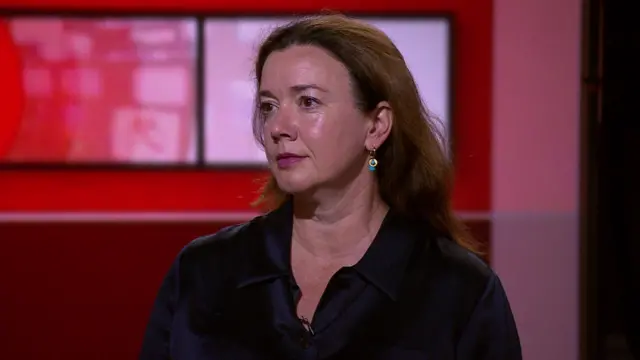 Stephanie Hare has long brunette hair, wears a black shirt and sits in the BBC studio