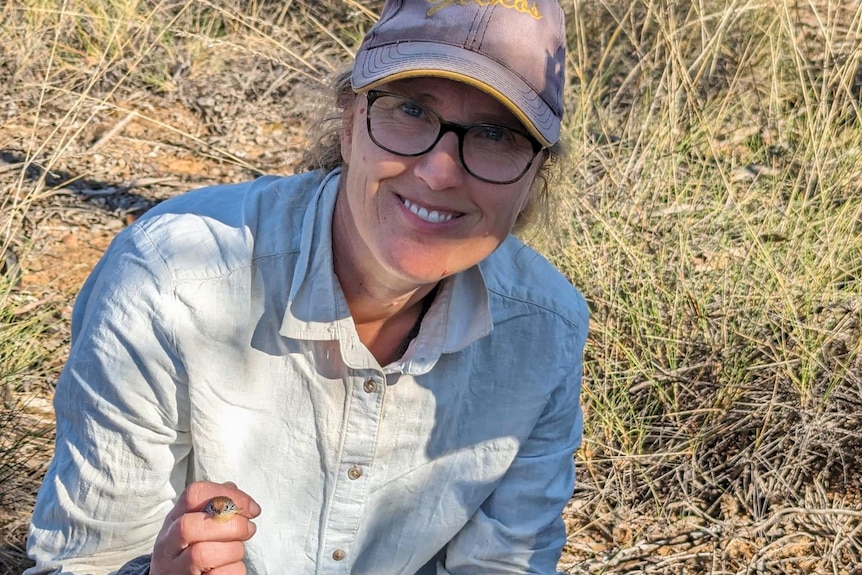 A woman smiles looking at the camera. She holds a small bird.