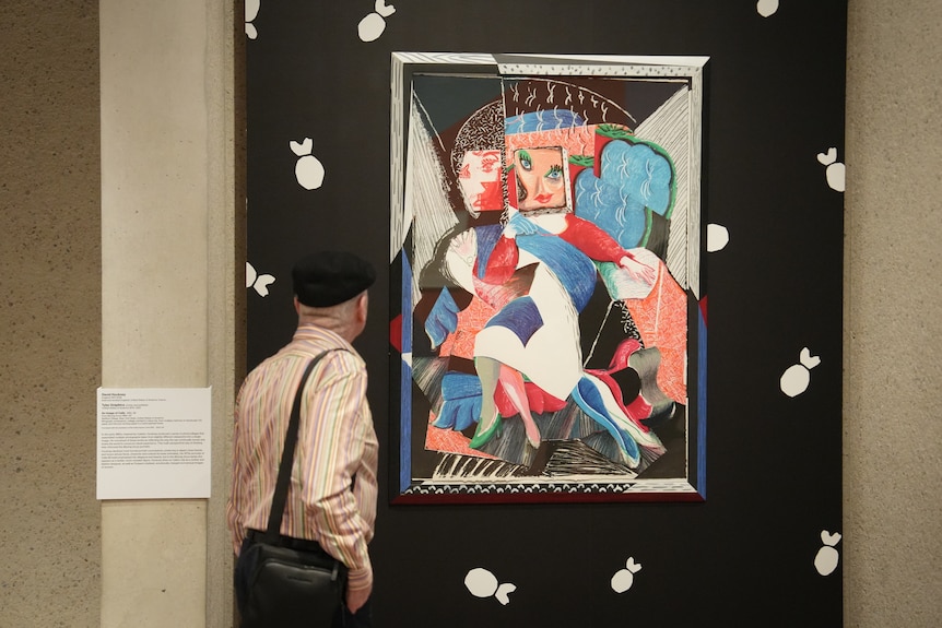 A man standing in front of a portrait of Hockney's friend Celia.