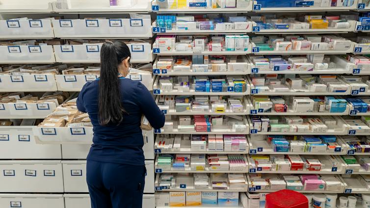 A pharmacist in front of shelves of medications.