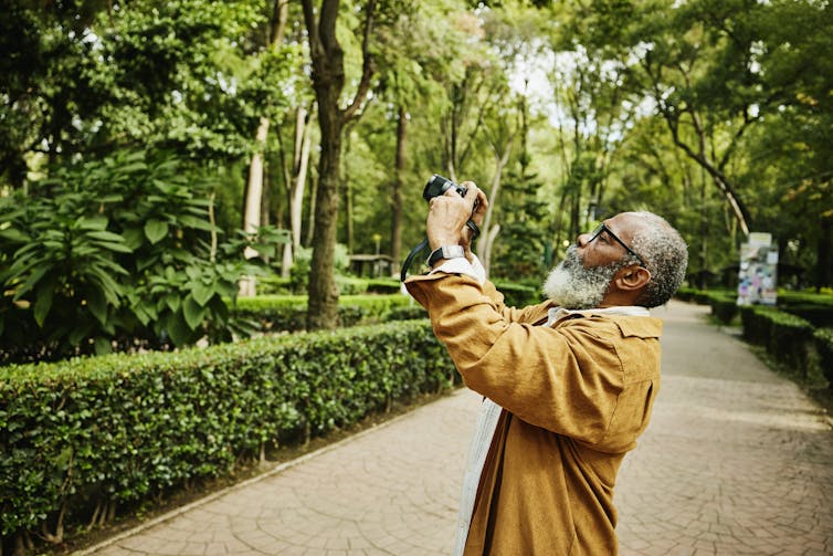Older man taking photos in a green city park