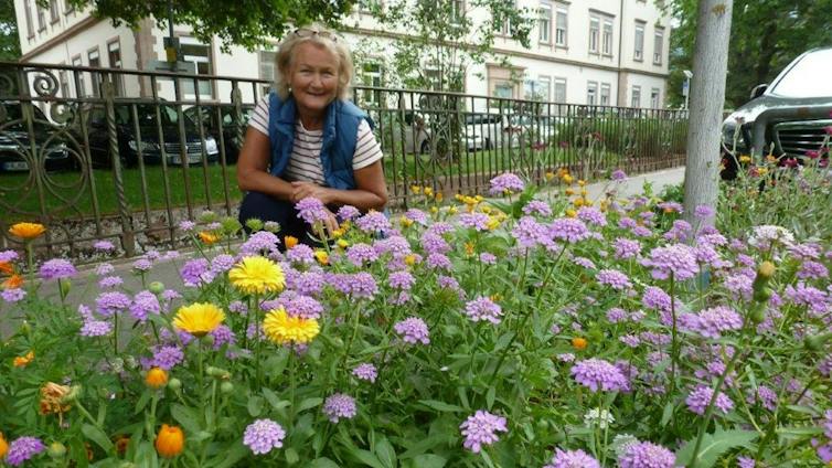 Woman kneels by flowerbeds in city street