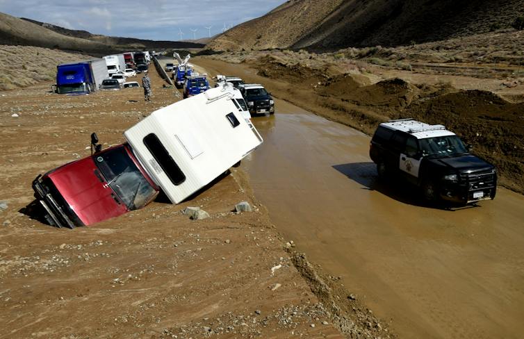 Several vehicles are tipped and trapped in mud up their windows along a highway.