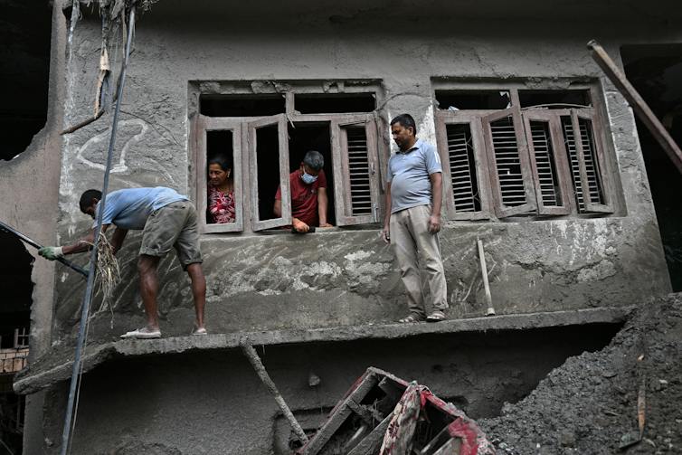 People stand on a board to reach second-floor windows of a home. The mud largely covers the first floor.