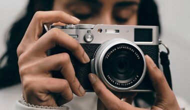 A person holds a silver and black digital camera with a Fujinon 23mm lens up to their face.