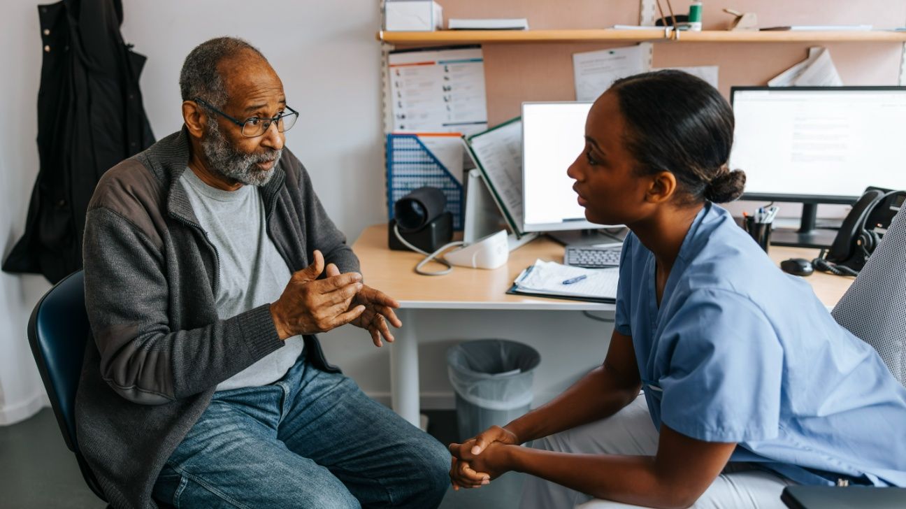 Older male speaking with a healthcare professional in a clinical setting
