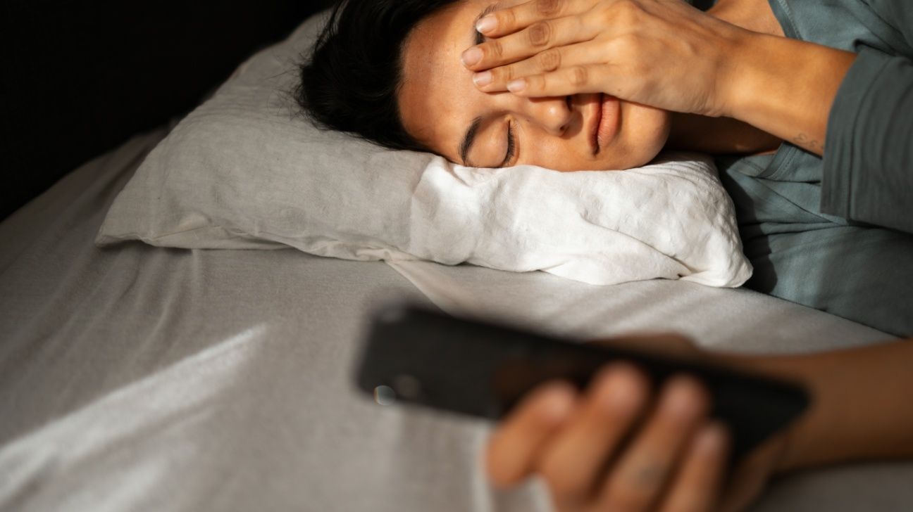 Female lays in bed with smartphone