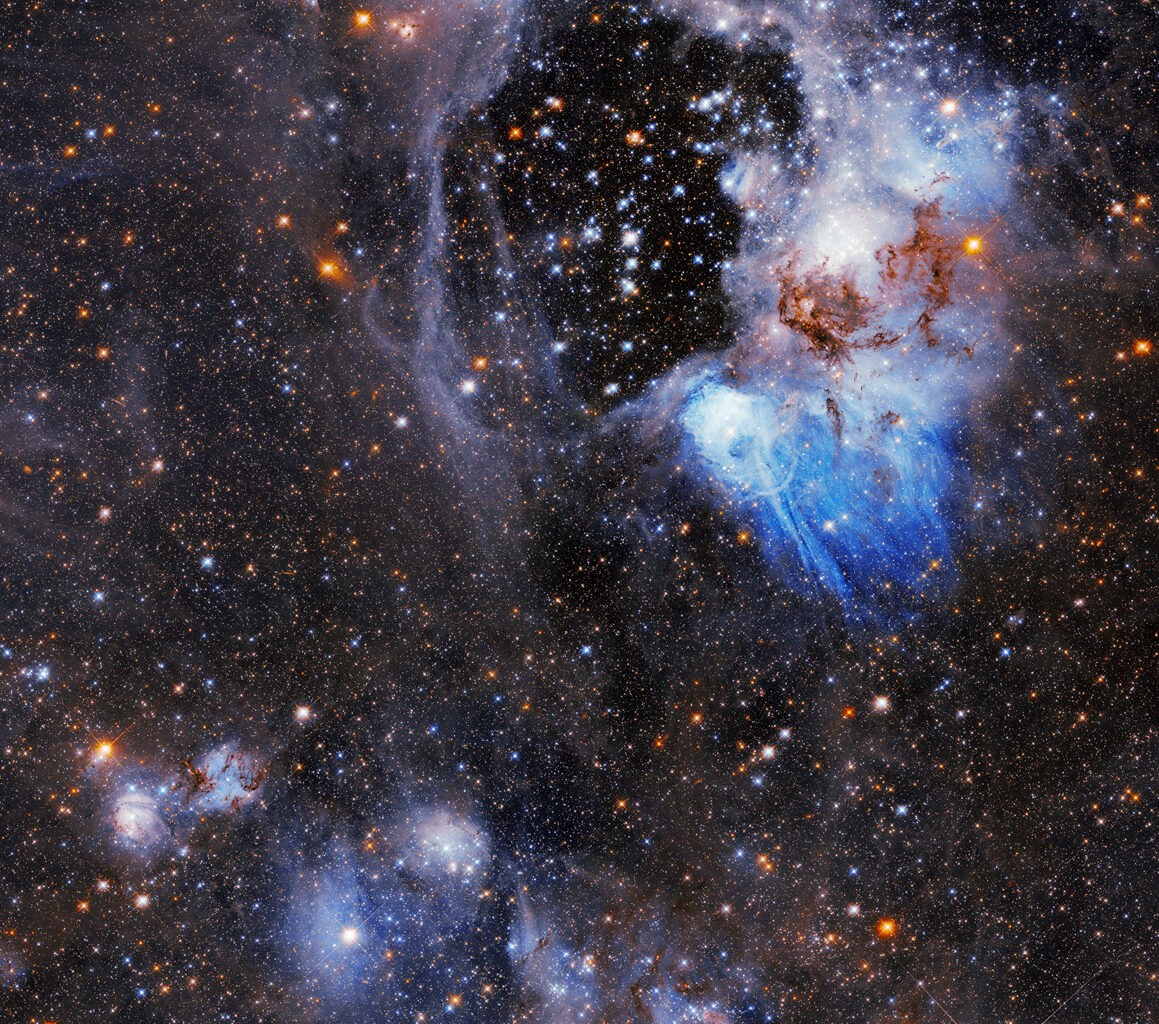 Blue and orange stars shine through a wispy bubble of gas; the center is mostly clear, but blue and gray tendrils snake throughout most of the rest of the image. The background of the image is filled with other stars.