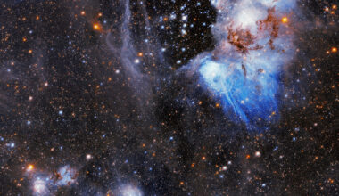 Blue and orange stars shine through a wispy bubble of gas; the center is mostly clear, but blue and gray tendrils snake throughout most of the rest of the image. The background of the image is filled with other stars.