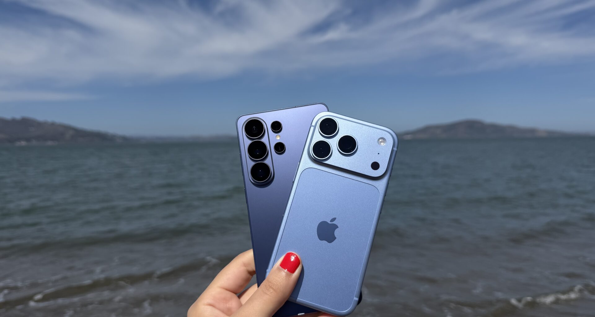 iPhone 18 Pro and Galaxy S26 Ultra on a beach with the ocean in the background.