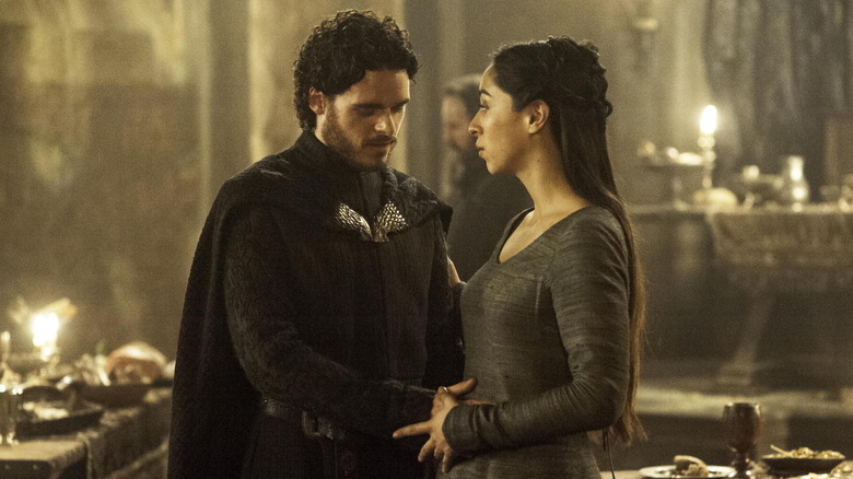 Richard Madden and Oona Chaplin as Rob and Talisa Stark, holding hands around her stomach in Game of Thrones.