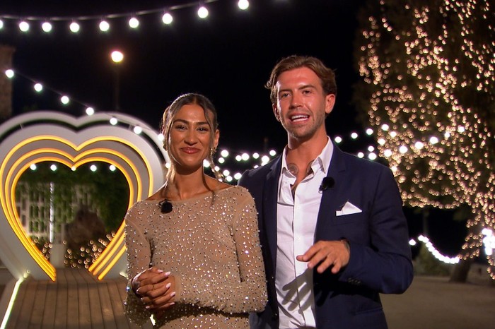 Love Island S13 Priya and Aidan stood next to each other in glamorous outfits, smiling ahead as they stand outside the villa.