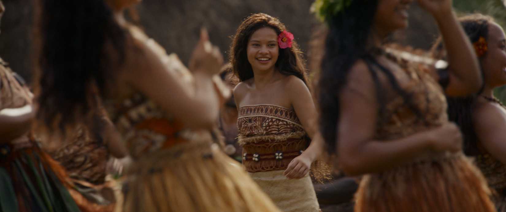 Moana (Catherine Laga'aia) smiles as dancers swirl around her in a production number from the 2026 live-action Moana