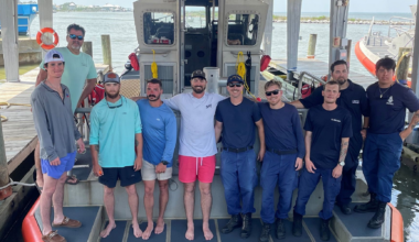 A group of people on a boat, several of them are wearing shirts with text reading "U.S. Coast Guard"