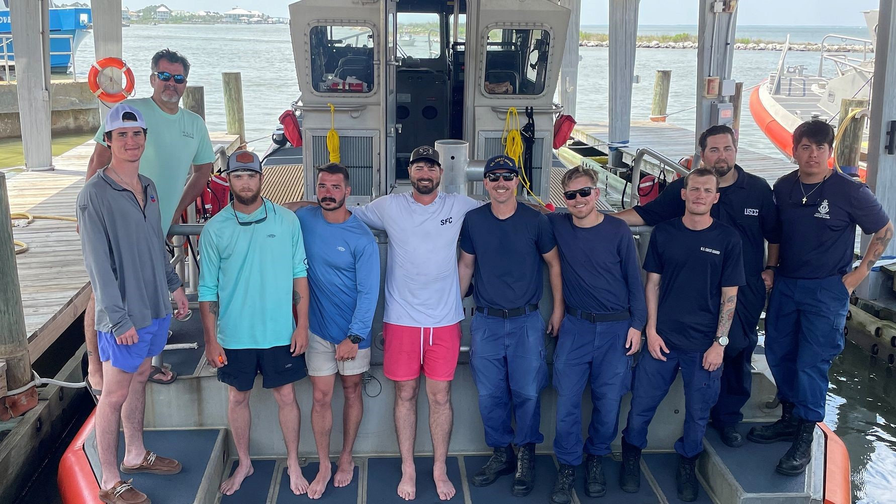 A group of people on a boat, several of them are wearing shirts with text reading "U.S. Coast Guard"