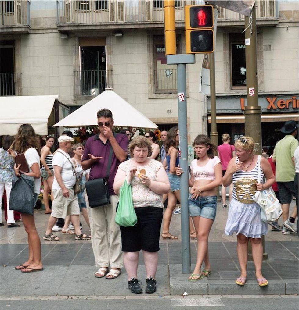 A mother and daughter waiting to cross a city street looking at a heavy set woman standing next to them.