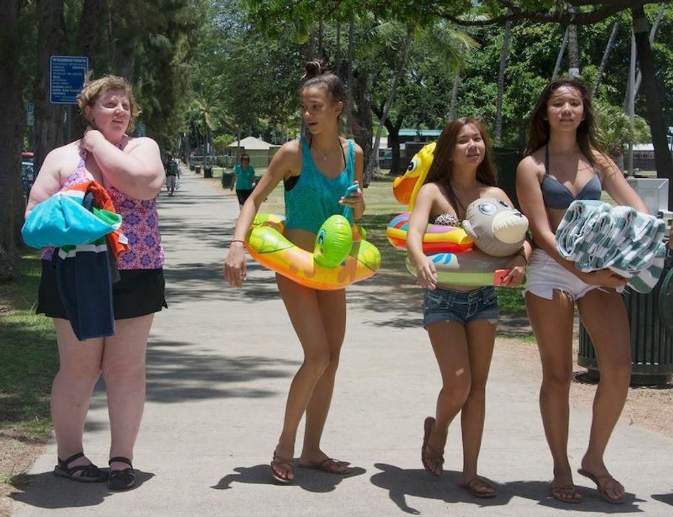 Three teenage girls wearing beach attire looking at a heavy set woman as they walk by.