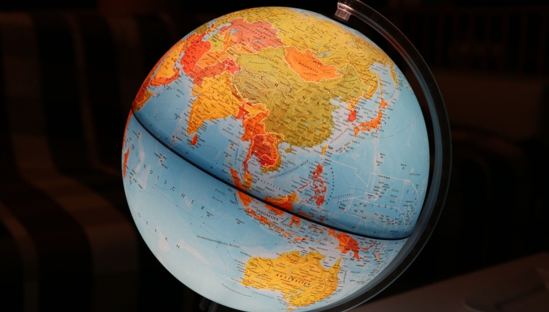 Blue and yellow physical globe showing Asia and Australia against a dark background