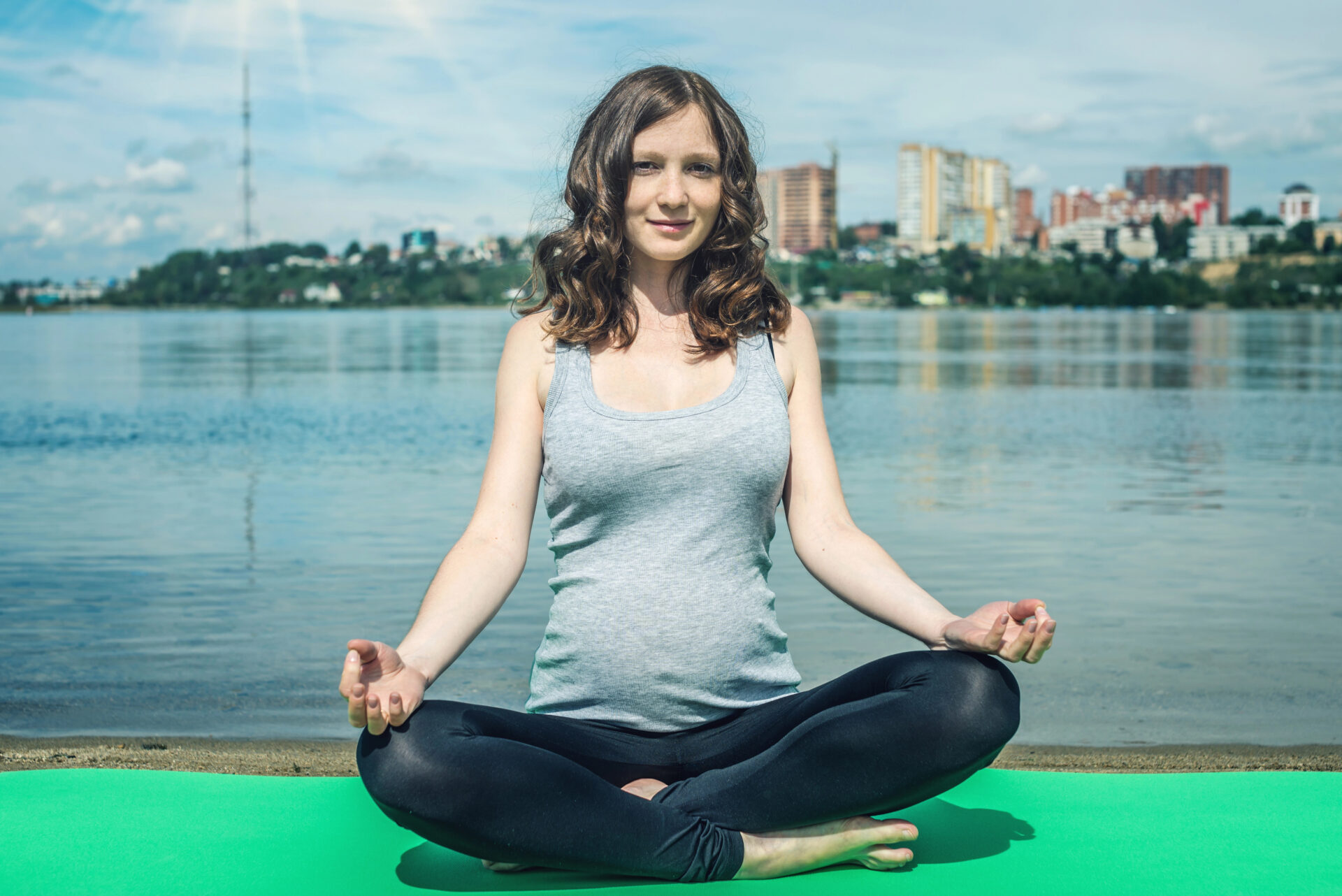 Pregnant woman sitting in front of water doing yoga