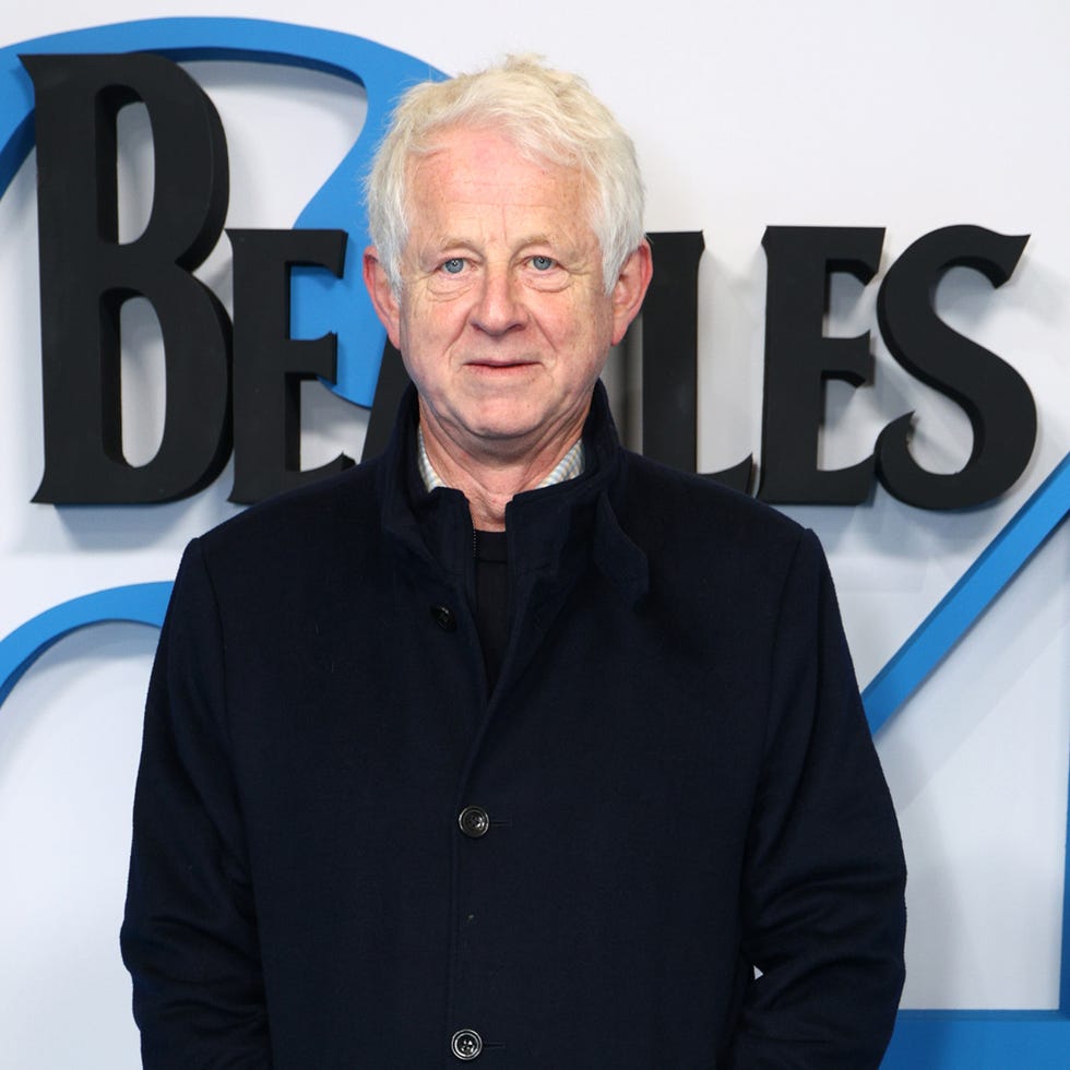 Richard Curtis richard curtis in front of a blue and white backdrop featuring beatles 64 and disney logos