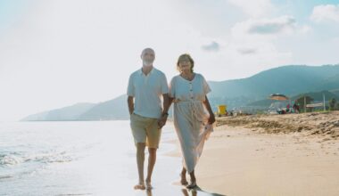 Happy senior couple enjoying their vacation, walking hand in hand along the ocean shoreline at sunset, reflecting love, companionship, and retirement joy
