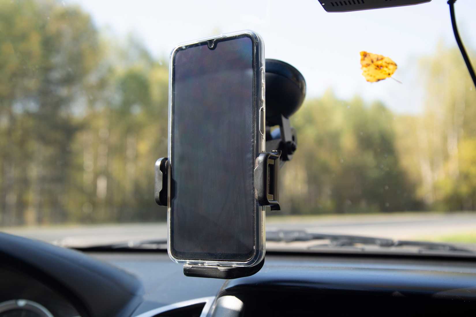A smartphone held vertically in a suction-cup car mount attached to the windshield.
