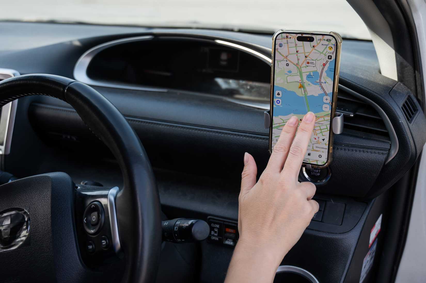 A person using a navigation map on a smartphone mounted to a car dashboard.