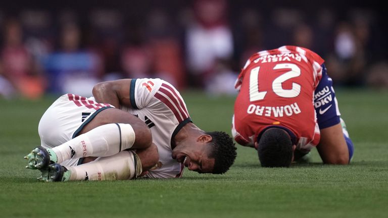 Real Madrid's Jude Bellingham and Atletico Madrid's Cristian Romero grimace on the ground after a collision during the derby