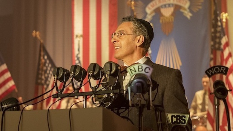 Rabbi Lionel Bengelsdorf wearing yarmulke and suit in front of microphones and American flag