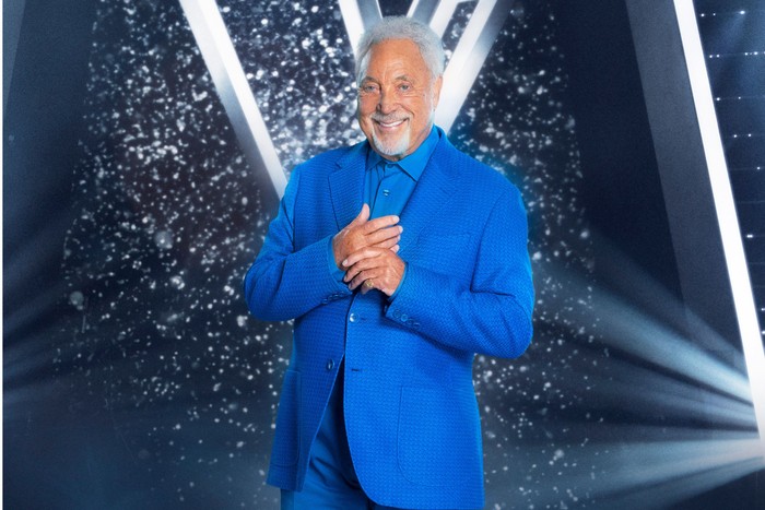 the-voice Sir Tom Jones wearing a bright blue suit, smiling ahead with his hands held close to his chest.