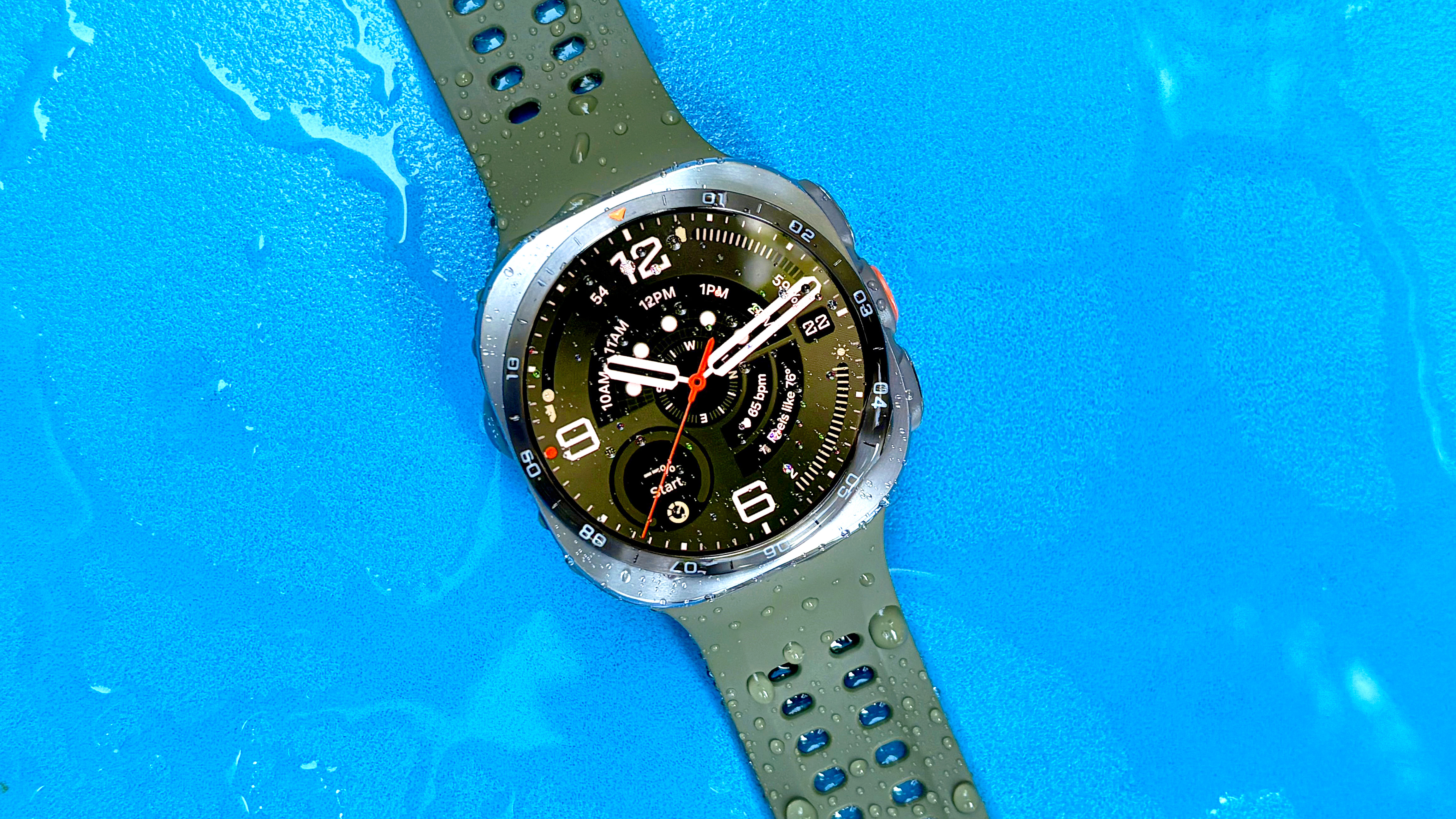 Close-up of a water-soaked Samsung Galaxy Watch Ultra 2 on a bright blue background
