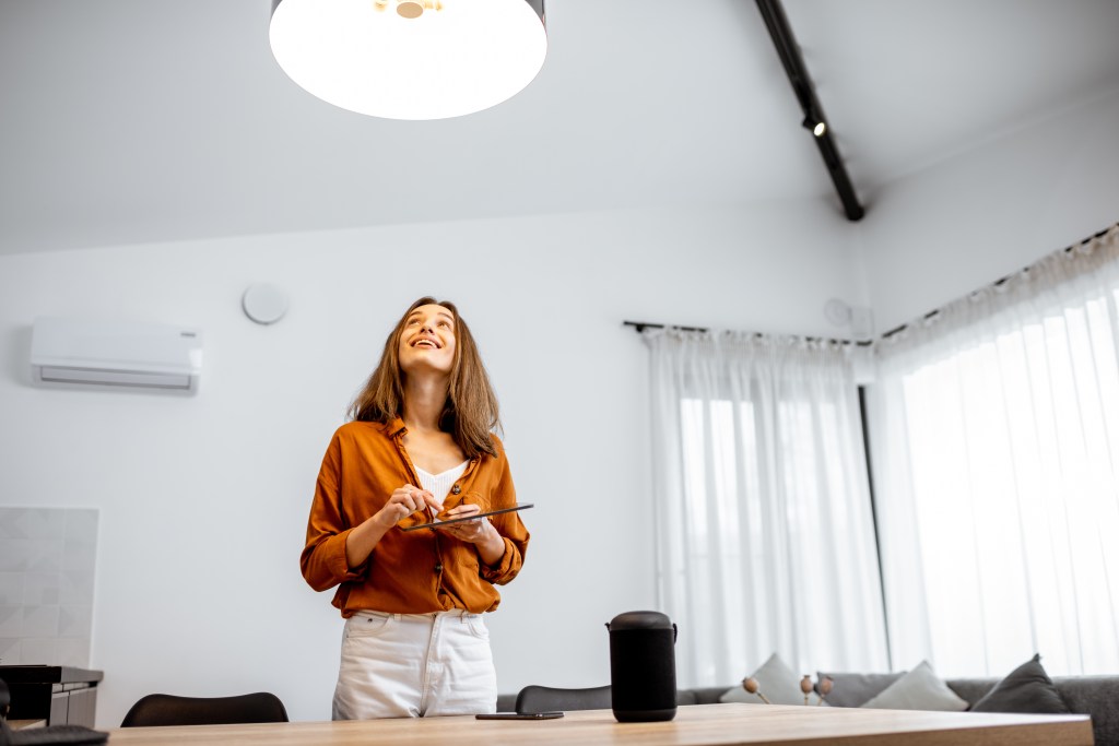 A woman uses a tablet to control a smart home light fixture.