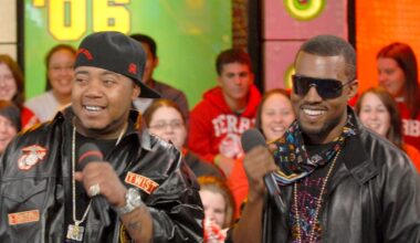 Kanye West wearing a patterned bandana, sunglasses, and a white jacket, partially covering his face with the collar.