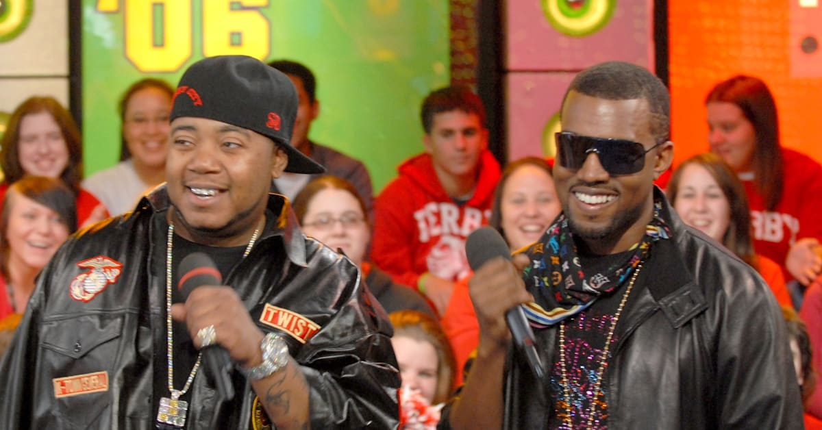 Kanye West wearing a patterned bandana, sunglasses, and a white jacket, partially covering his face with the collar.